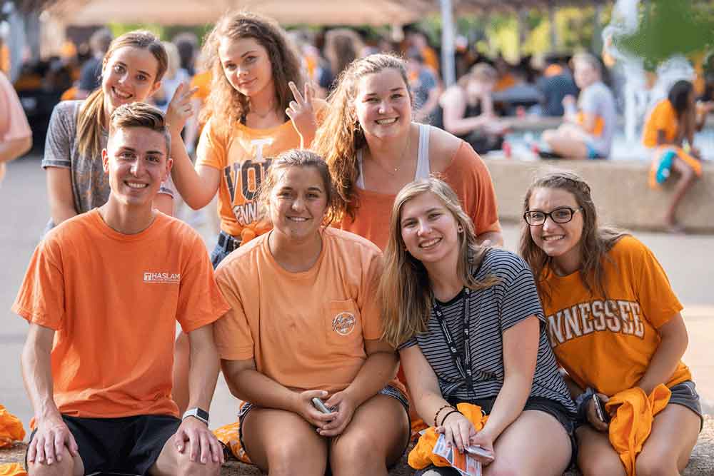 a group of smiling students gather on campus wearing orange.