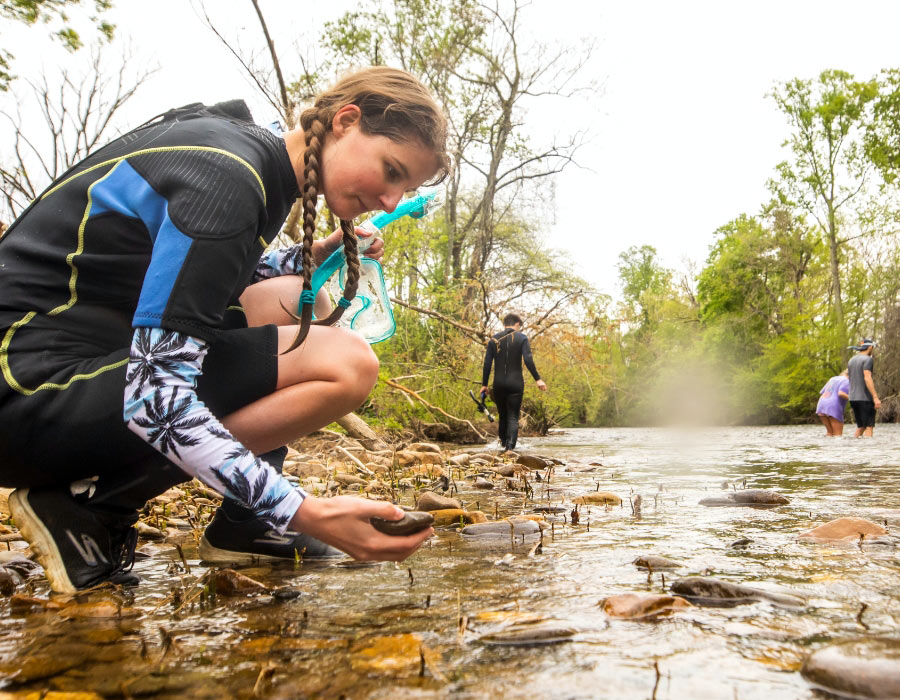 students wearing wetsuits work explore microbiology in the river
