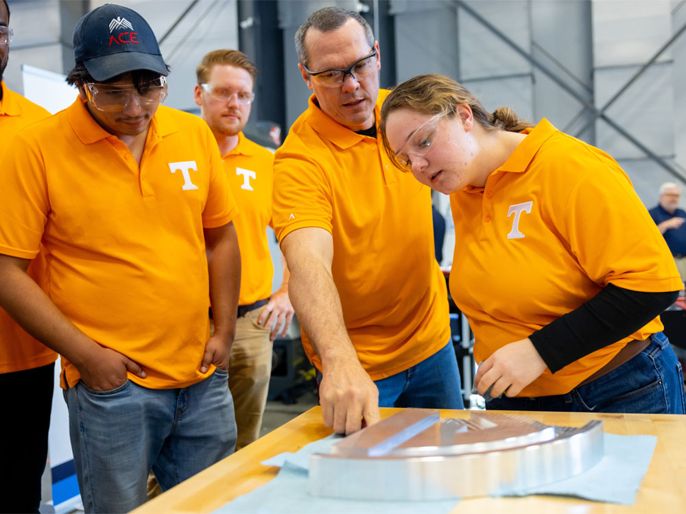 a team of students look over an aluminum part that has been recently fabricated