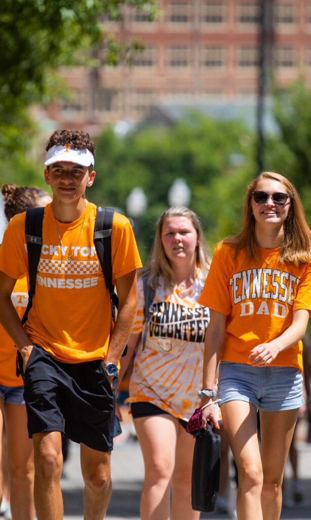 a group of students walk through the middle of campus proudly wearing orange