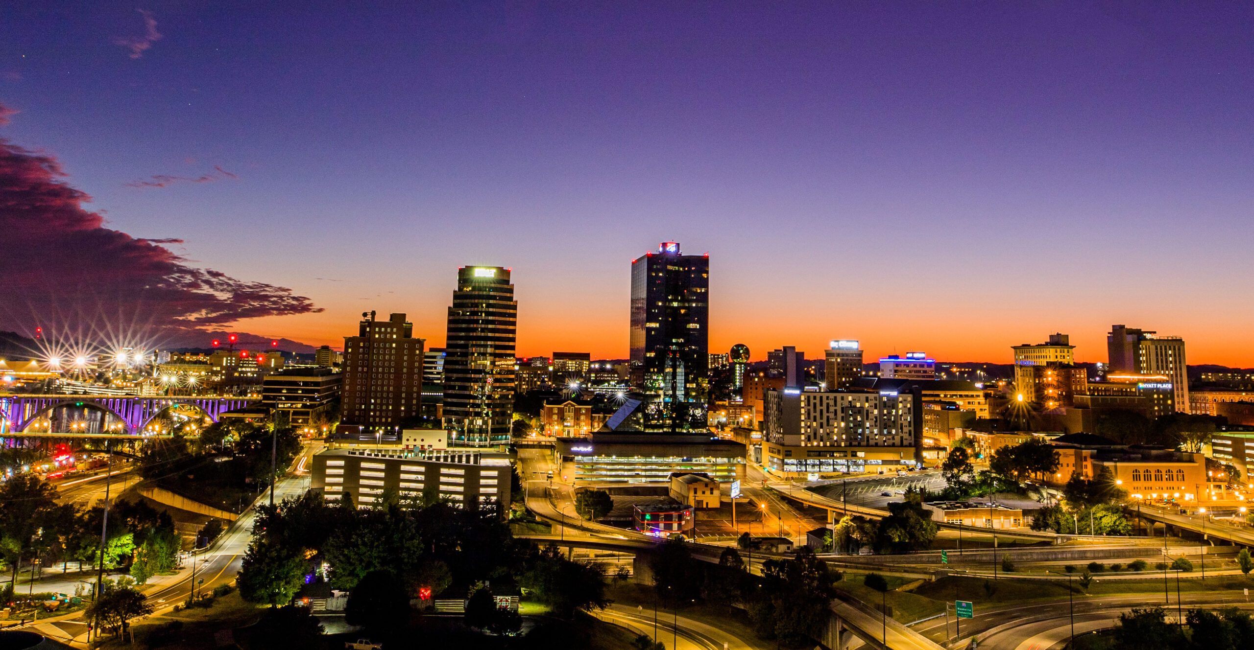 a wide shot of downtown Knoxville lit up at night with an orange sunset glowing in the background