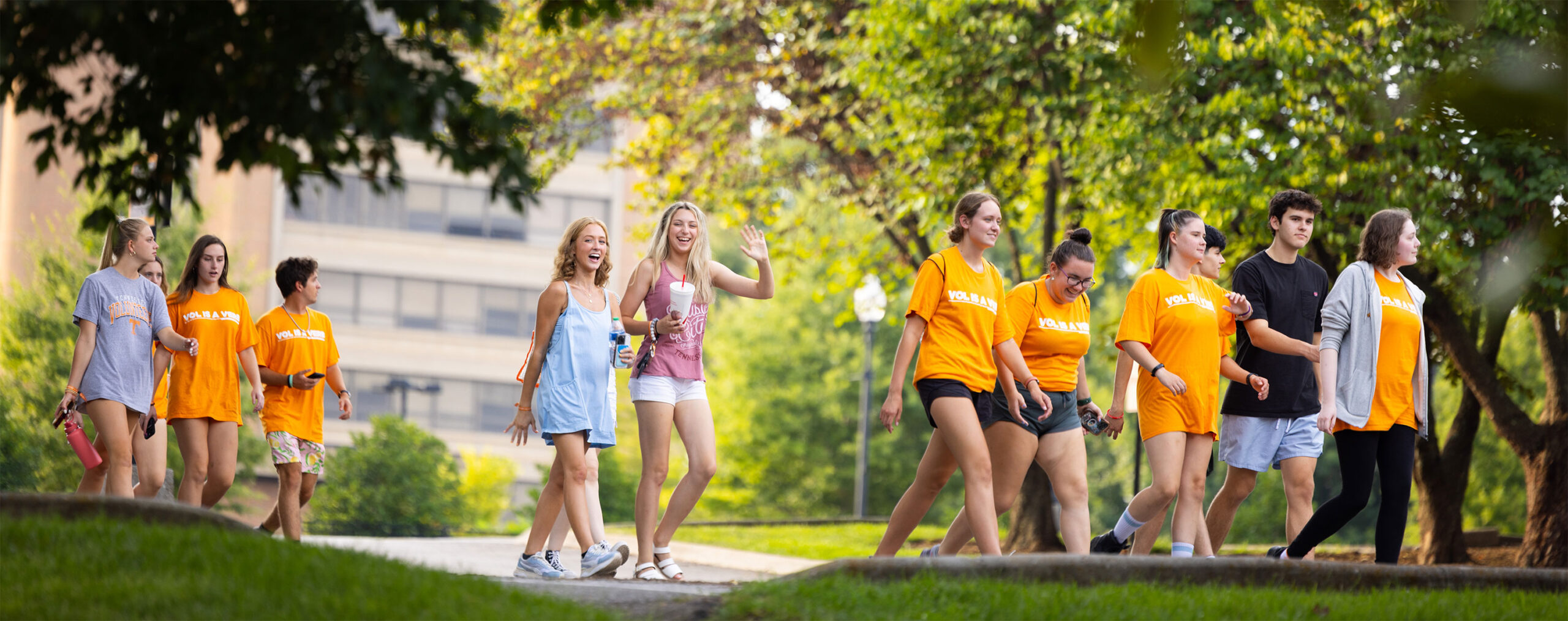 Students walk through a lush campus in early spring wearing bright orange shirts