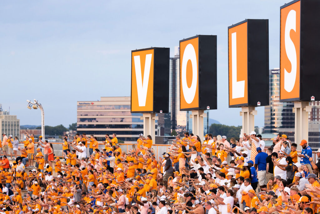 a packed stadium of orange dressed fans sit in front of the giant Vols letters that sit atop Neyland Stadium