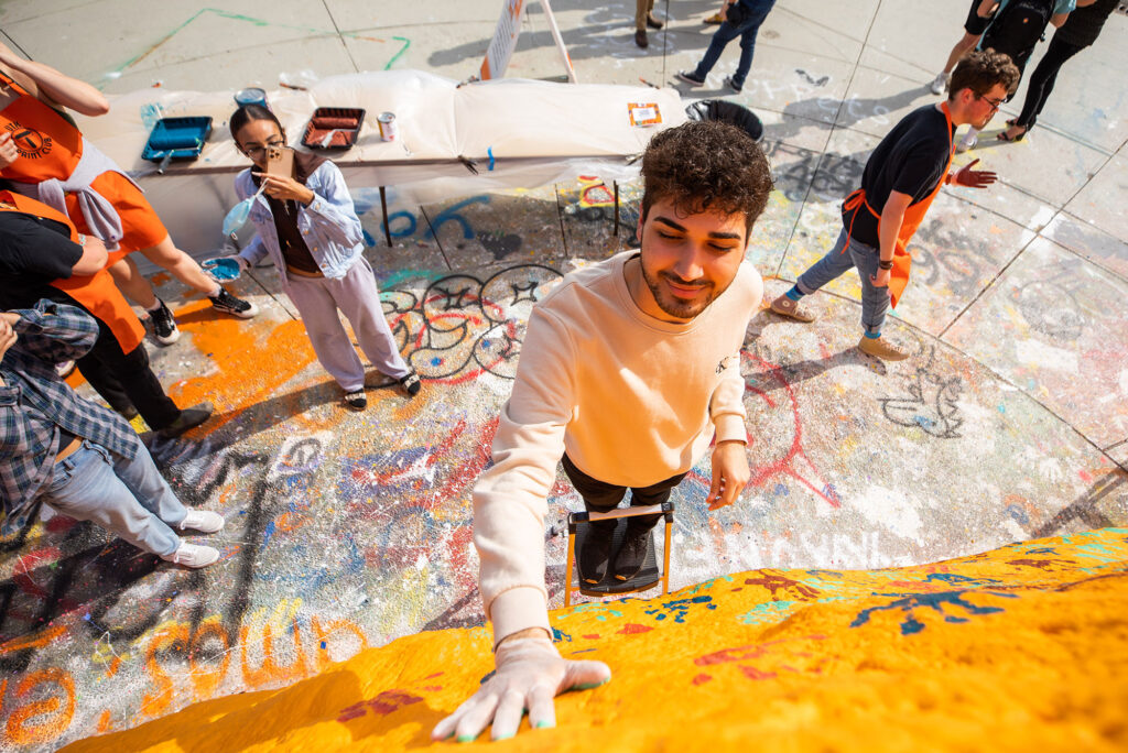 students paint the rock bright orange with colorful handprints