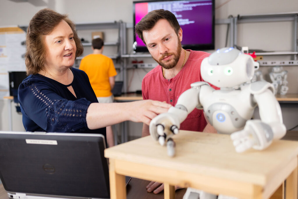 a vice chancellor and a student discuss how an AI robot works inside a lab