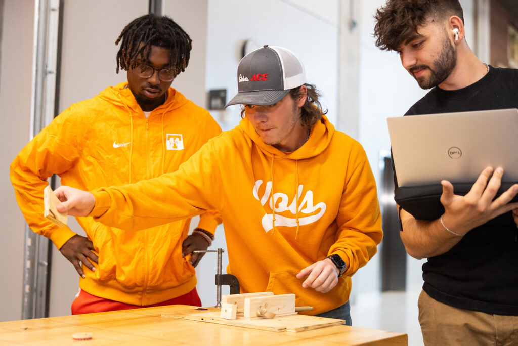 Three students work on a propulsion device dressed in bright UT orange while working on a laptop
