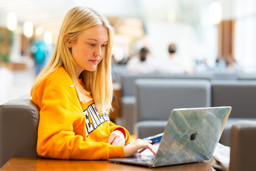 a student sits on campus working independently on a laptop