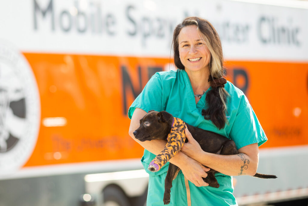 A student holds a puppy outside of the mobile spay and neuter clinic vehicle