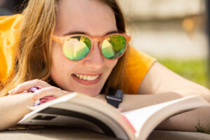 A girl wearing orange sunglasses reads a book